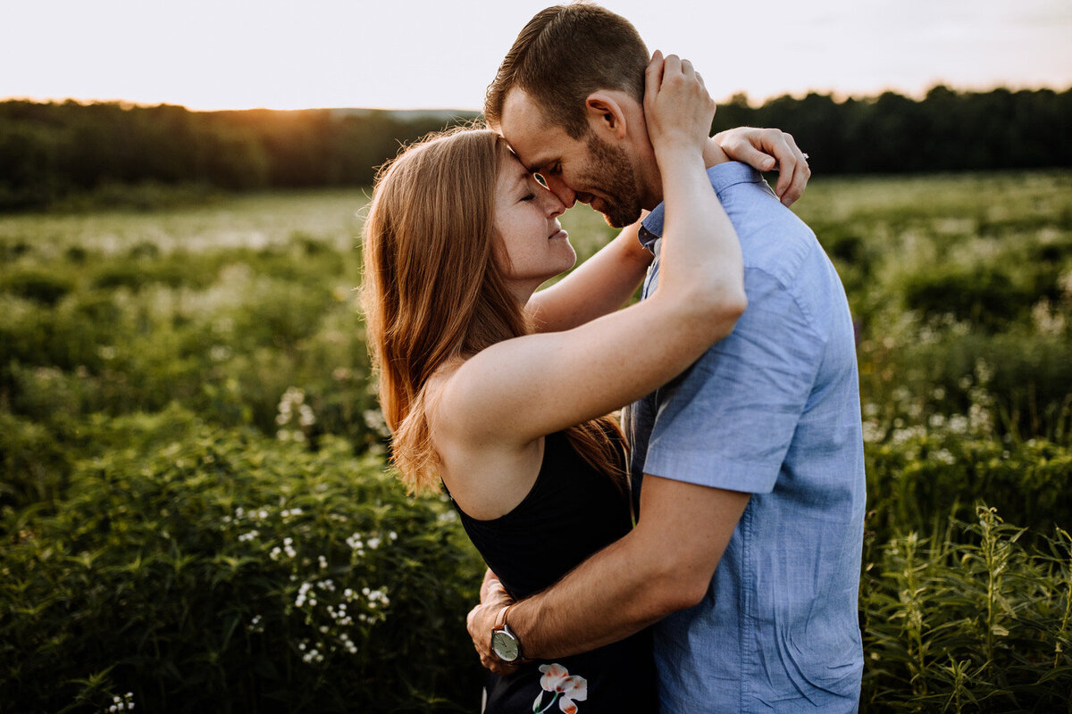 Bride and groom holding hands looking at each other while standing in front of rolling hills with the sunlight coming down on them