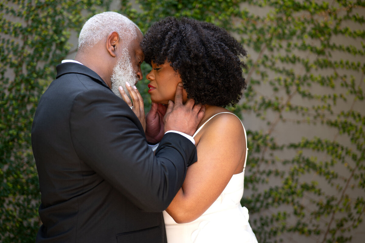 A newlywed couple with their hands on each other's faces about to kiss 