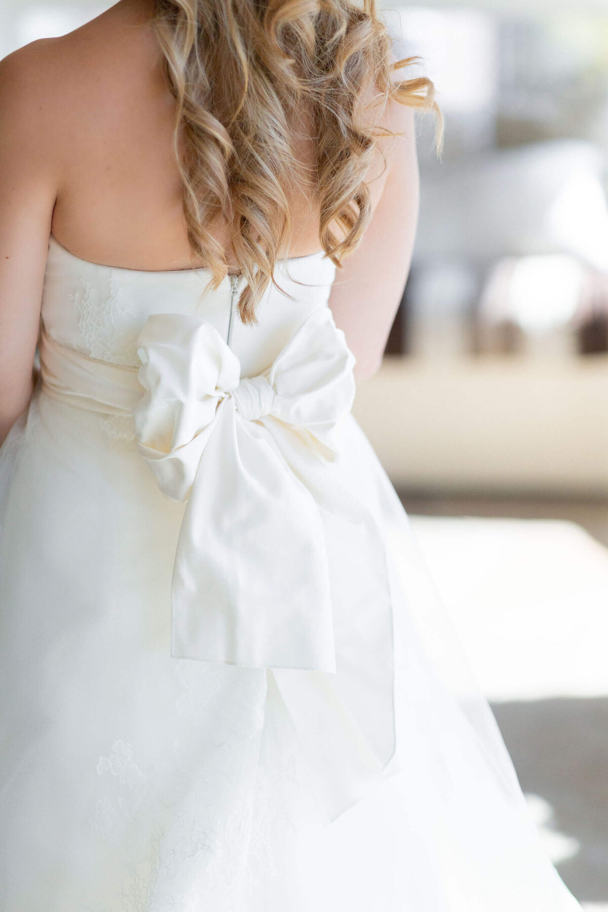 bride seen from behind, her hair drapes down over her shoulders, exposed by her strapless dress, with a large bow at her lower back