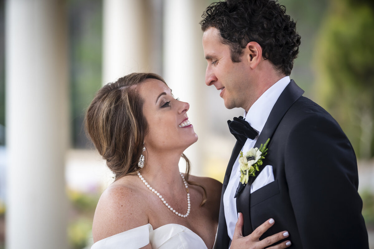 Bride looking into grooms eyes with hand on chest.