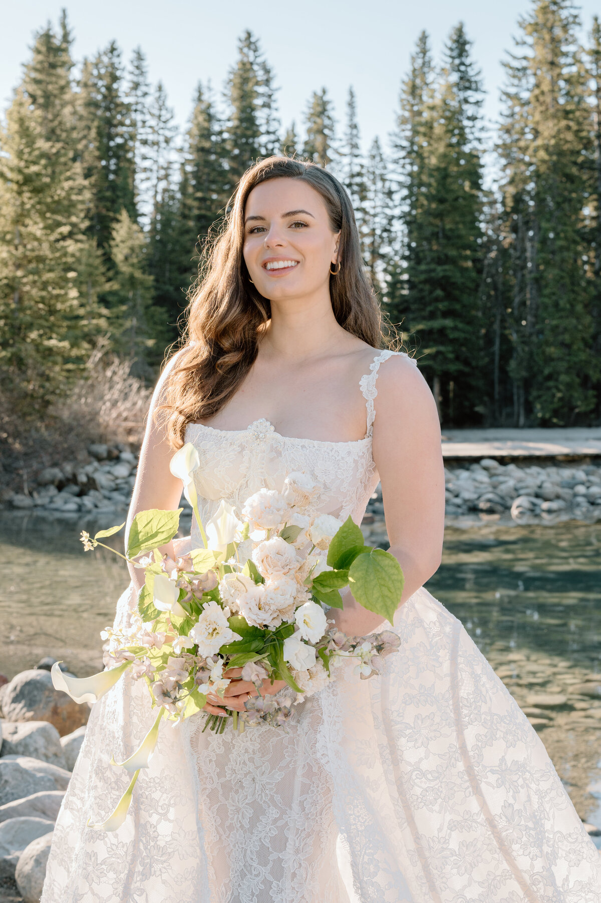Bridal portrait with white bouquet by forest river in Lake Louise