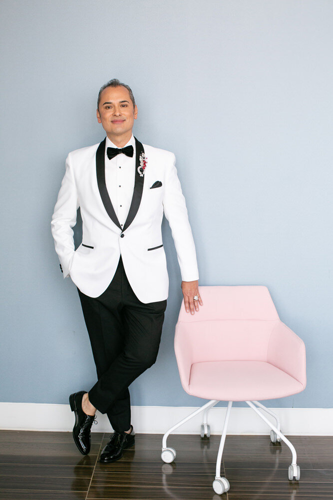 A groom standing next to a light pink chair