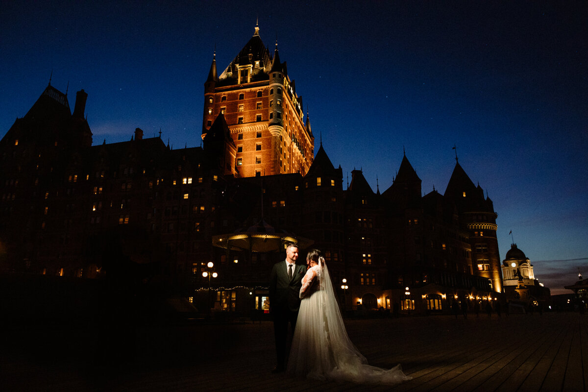 newlyweds-side-by-side-at-night-time-on-terrace-dufferin-in-front-of-the-chateau-frontenac-in-quebec-city-1