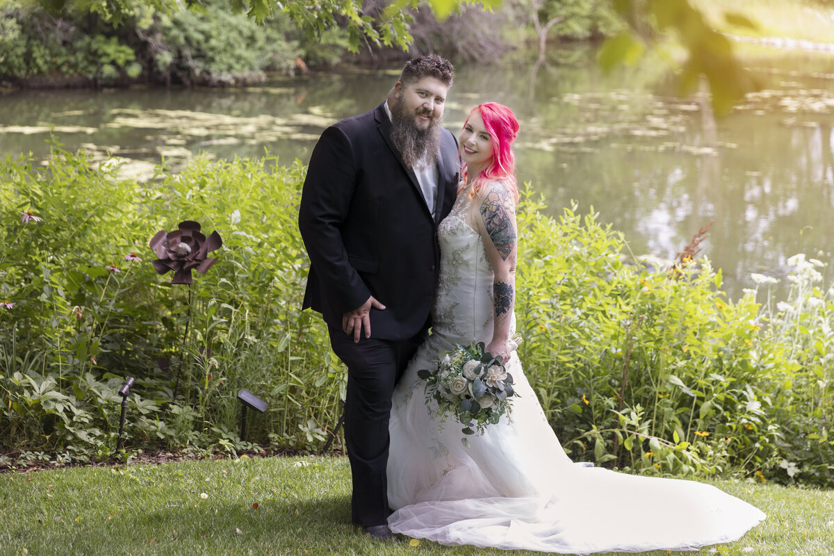 Bride and groom stand in front of a pond