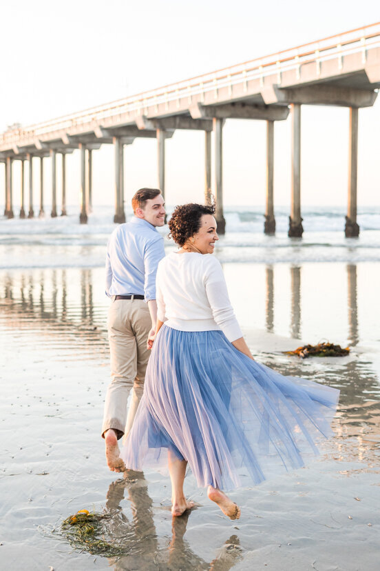 engaged-couple-running-toward-Scripps-Pier-San-Diego