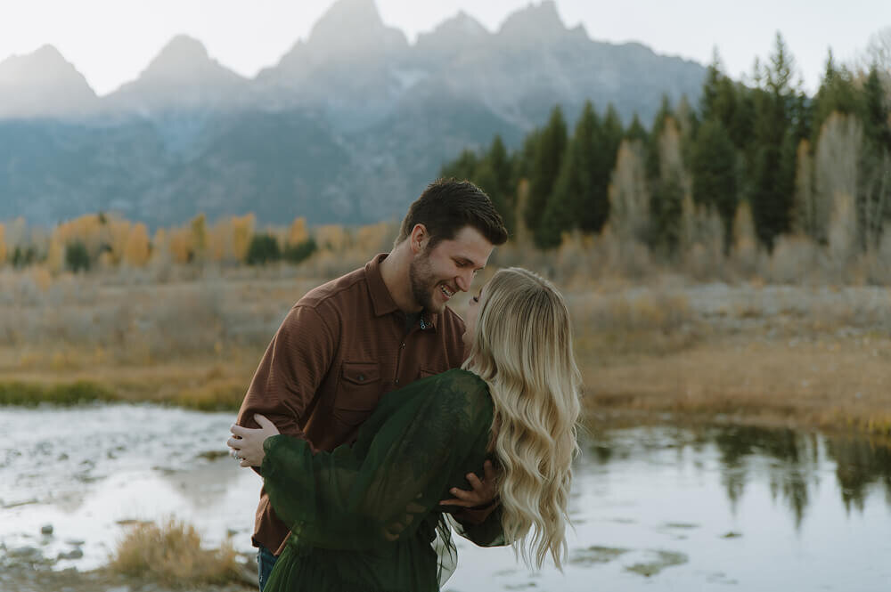A man slightly dips his fiancé as they look into each others eyes. Behind them is a stunning view of the Tetons. 