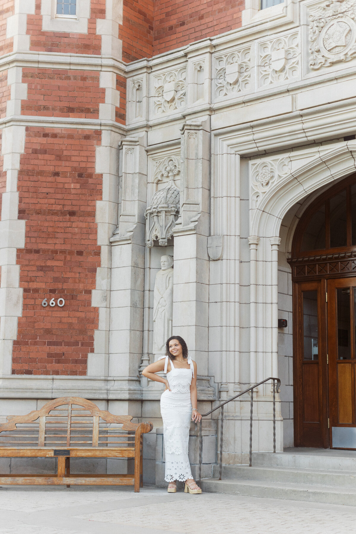 young woman in white dress poses in front of evans hall at the university of oklahoma