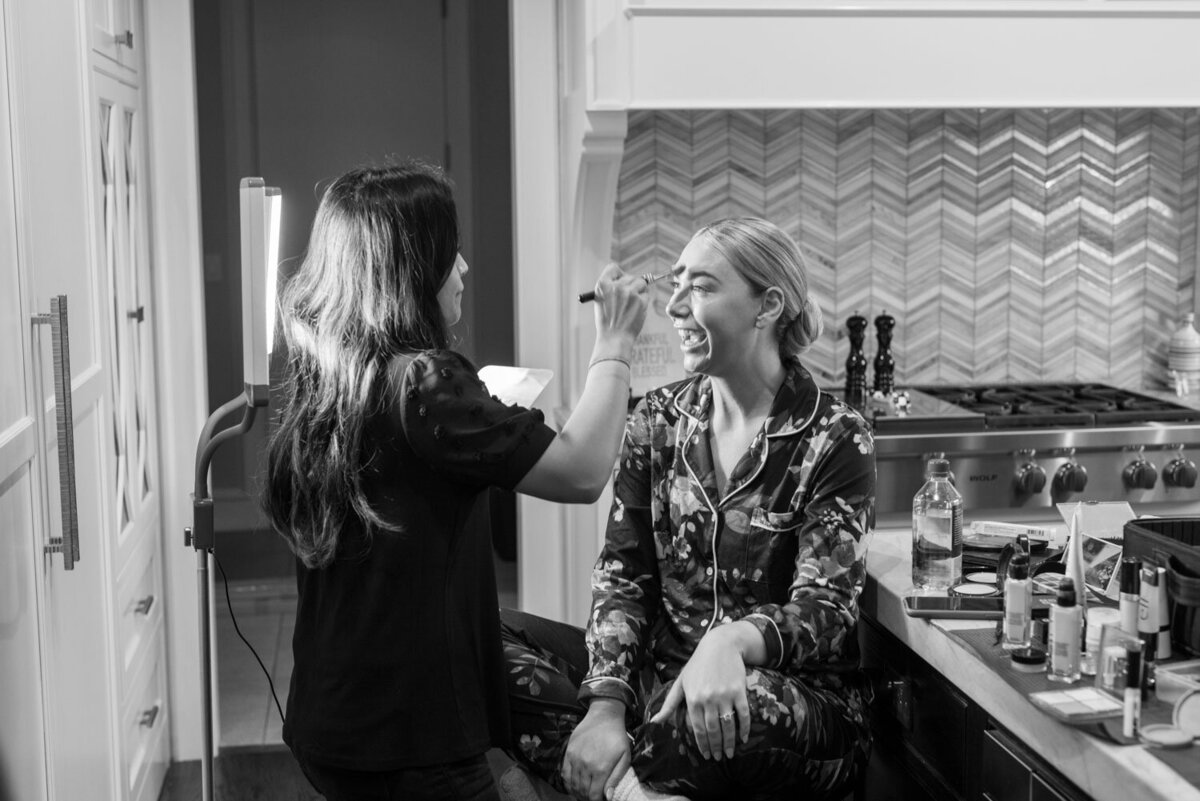 A woman is getting her makeup done by a makeup artist in a black and white photo.