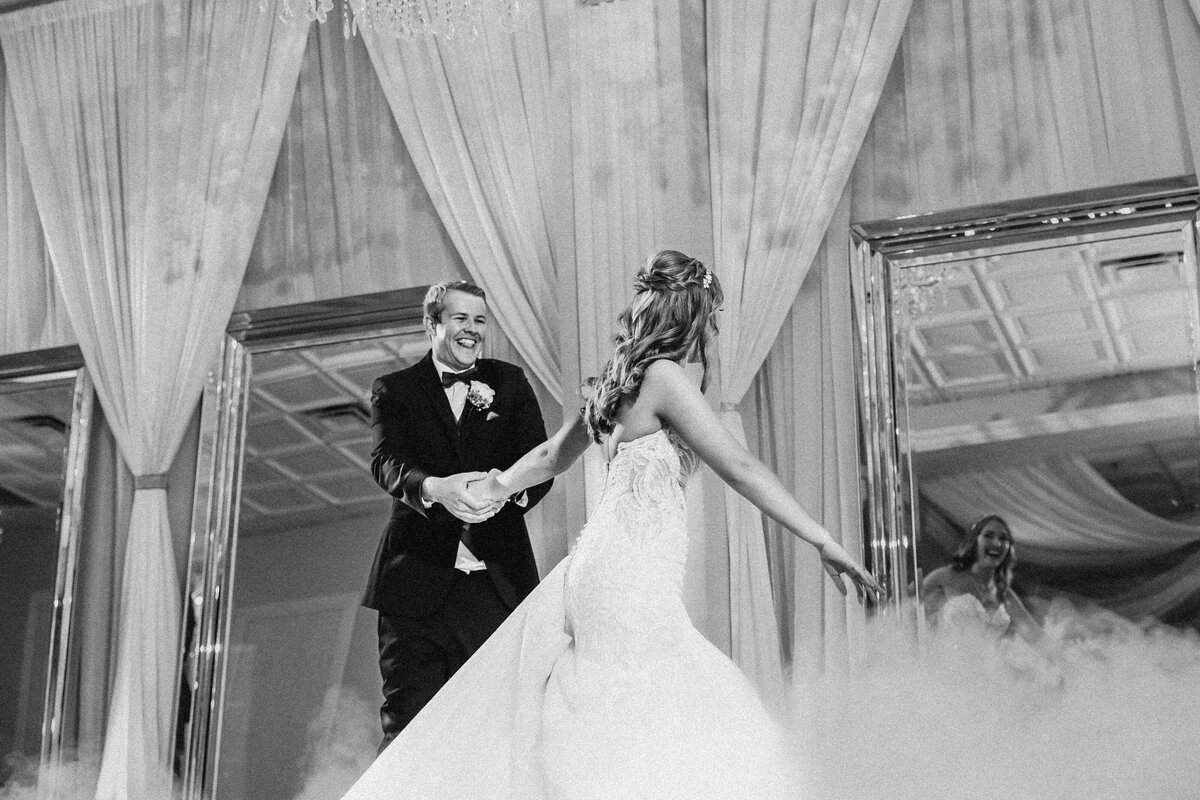 Groom laughs as he spins the bride across the dance floor, surrounded by fog and chandeliers in St. Augustine wedding venue.