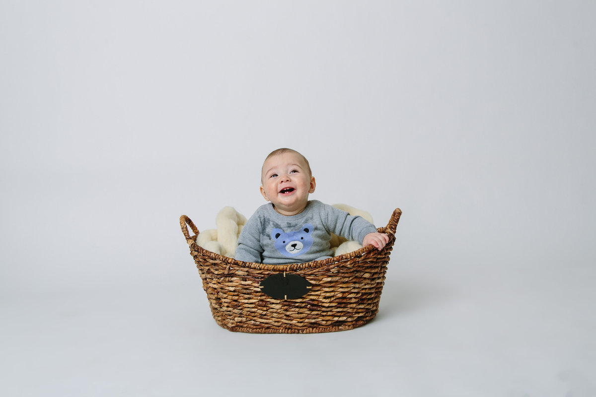In studio photography session of baby sitting in a basket and smiling.