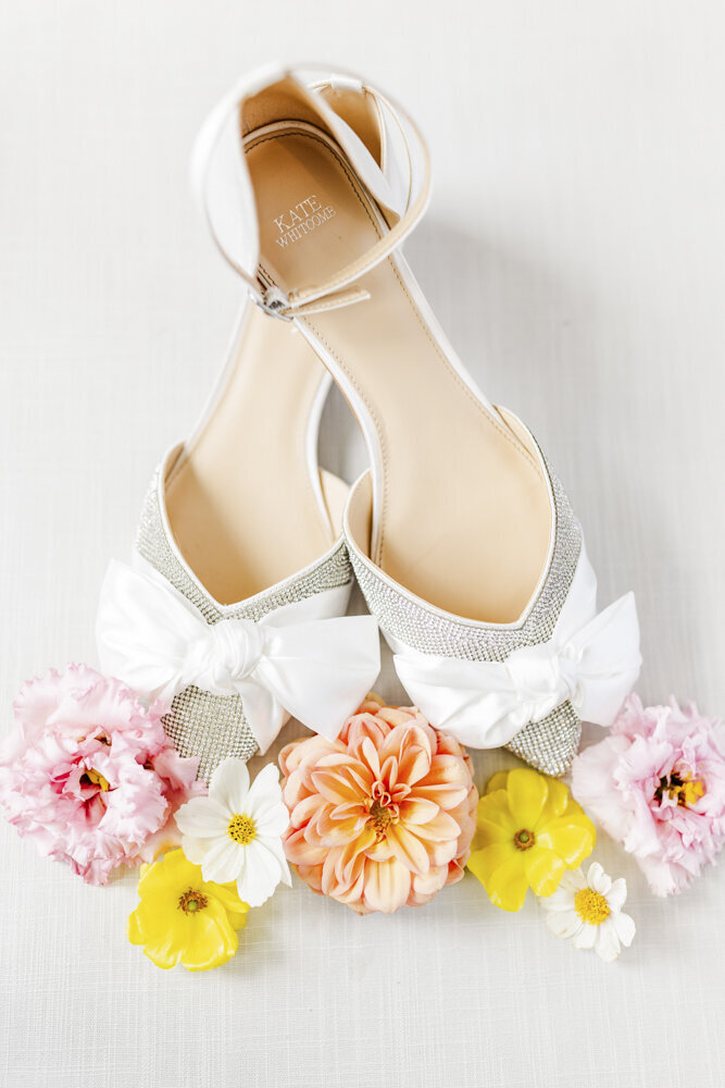 close up of white bridal shoes next to colorful flowers