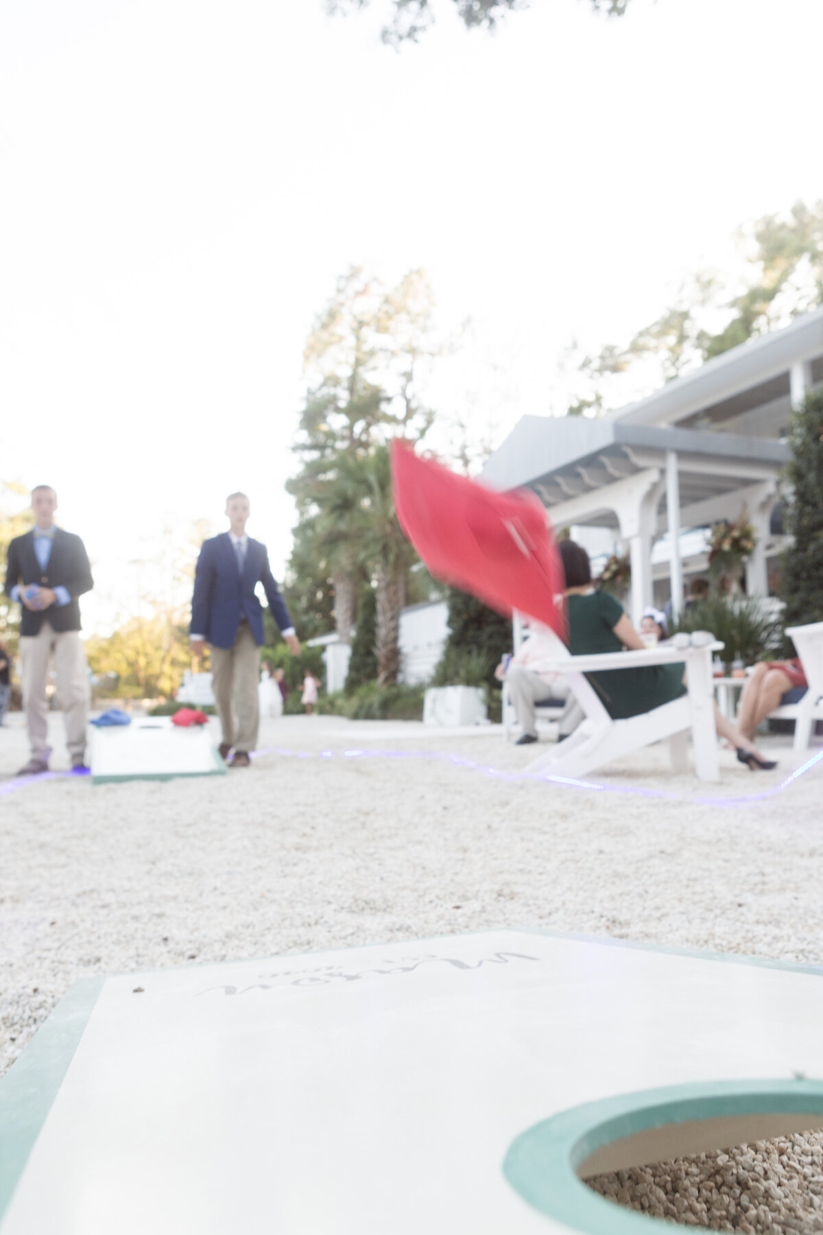 Guests of the wedding enjoy a game of cornhole at the wedding reception at Little Point Clear in Point Clear, Alabama.