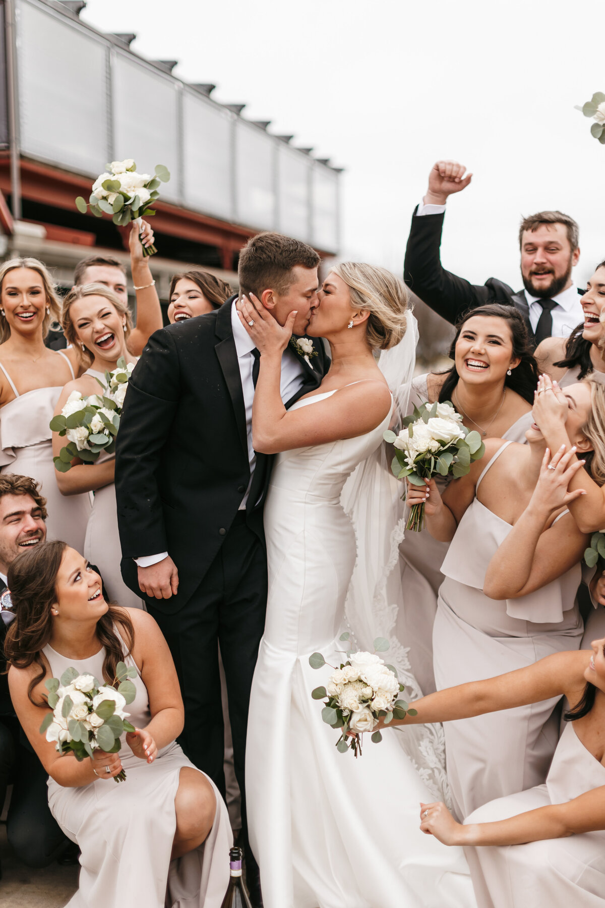 couple kissing with wedding party