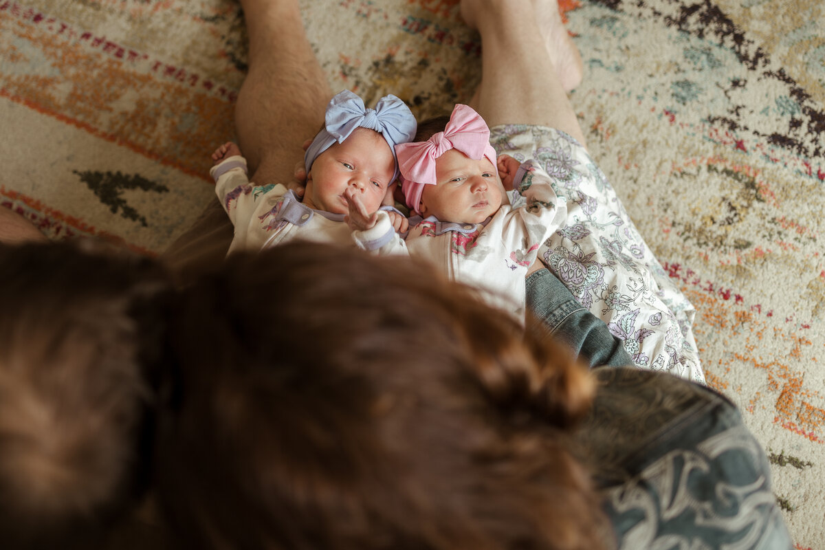 Mom and dad holding newborn twin baby girls with pink and purple bow in matching sleepers in firestone colorado