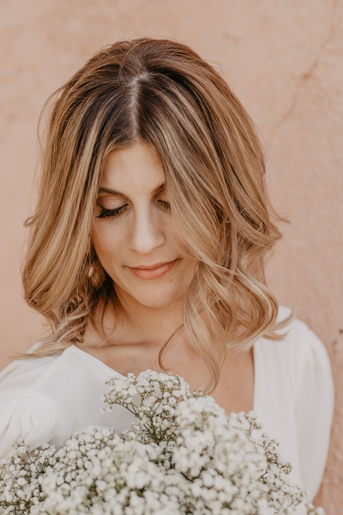 jackson wyoming photographer captures beautiful bride in a white sleeved dress looking down at her all white wedding bouquet for her grand teton wedding
