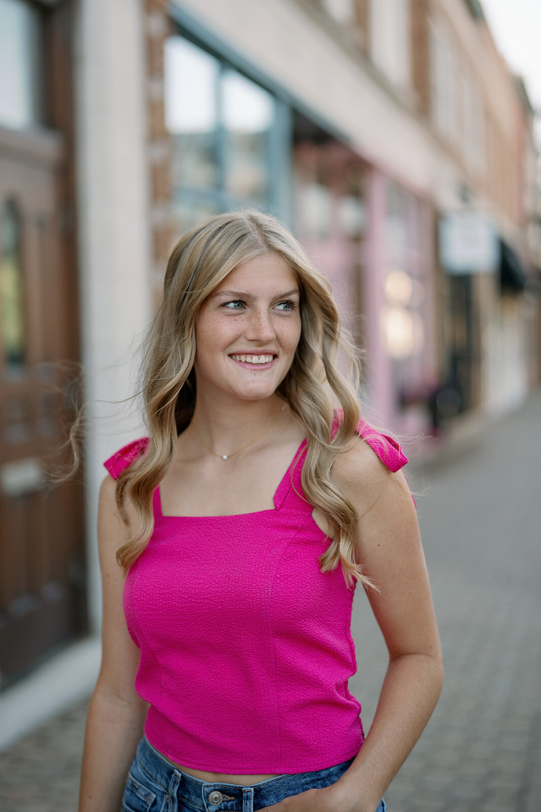 Senior girl smiling over her shoulder in front of a Holland Michigan storefront during her senior portrait shoot.