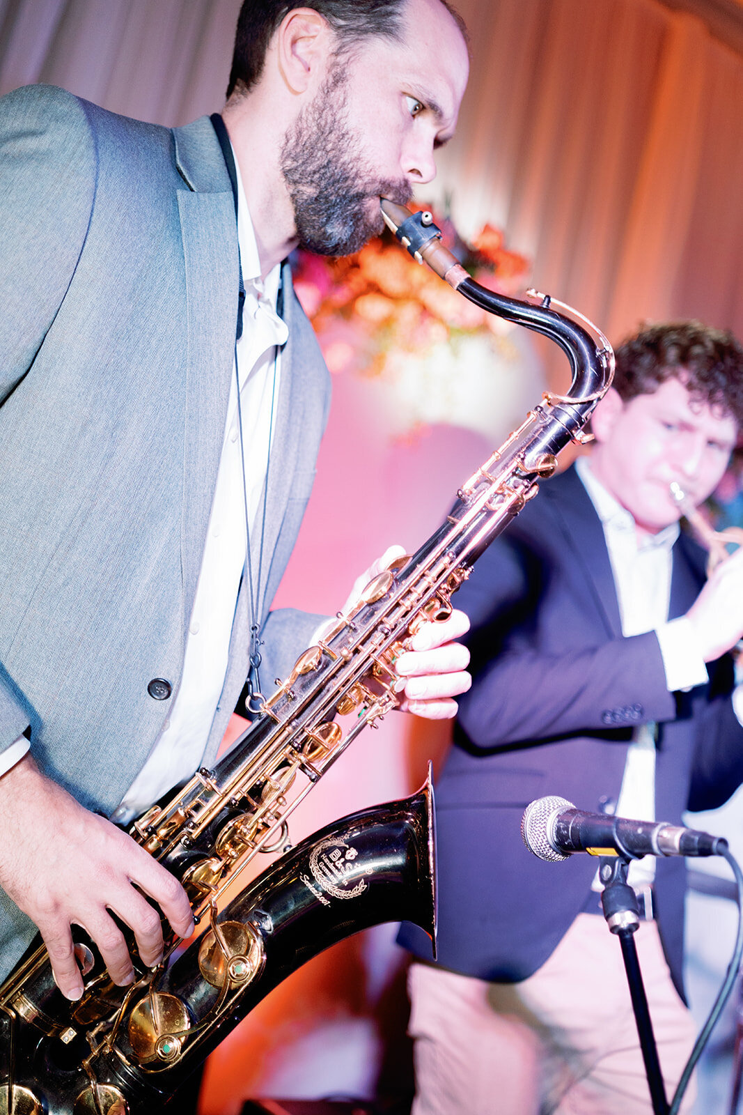 Saxophonist and trumpeter performing on stage at Callie and Hayes’ Burritt on the Mountain wedding reception under colorful stage lighting.