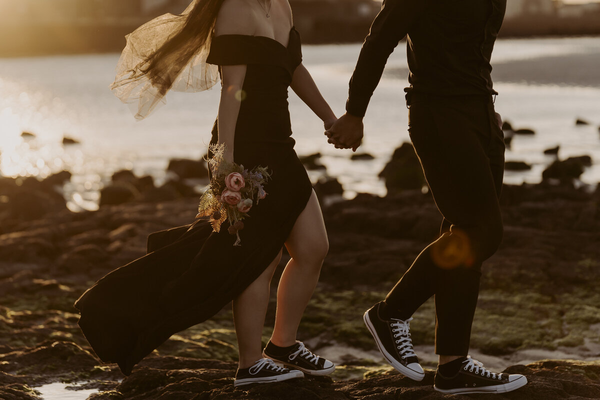 the bride holds her bouquet while walking hand in hand with the groom in the shore of Jeju Island showing  their converse all star shoes