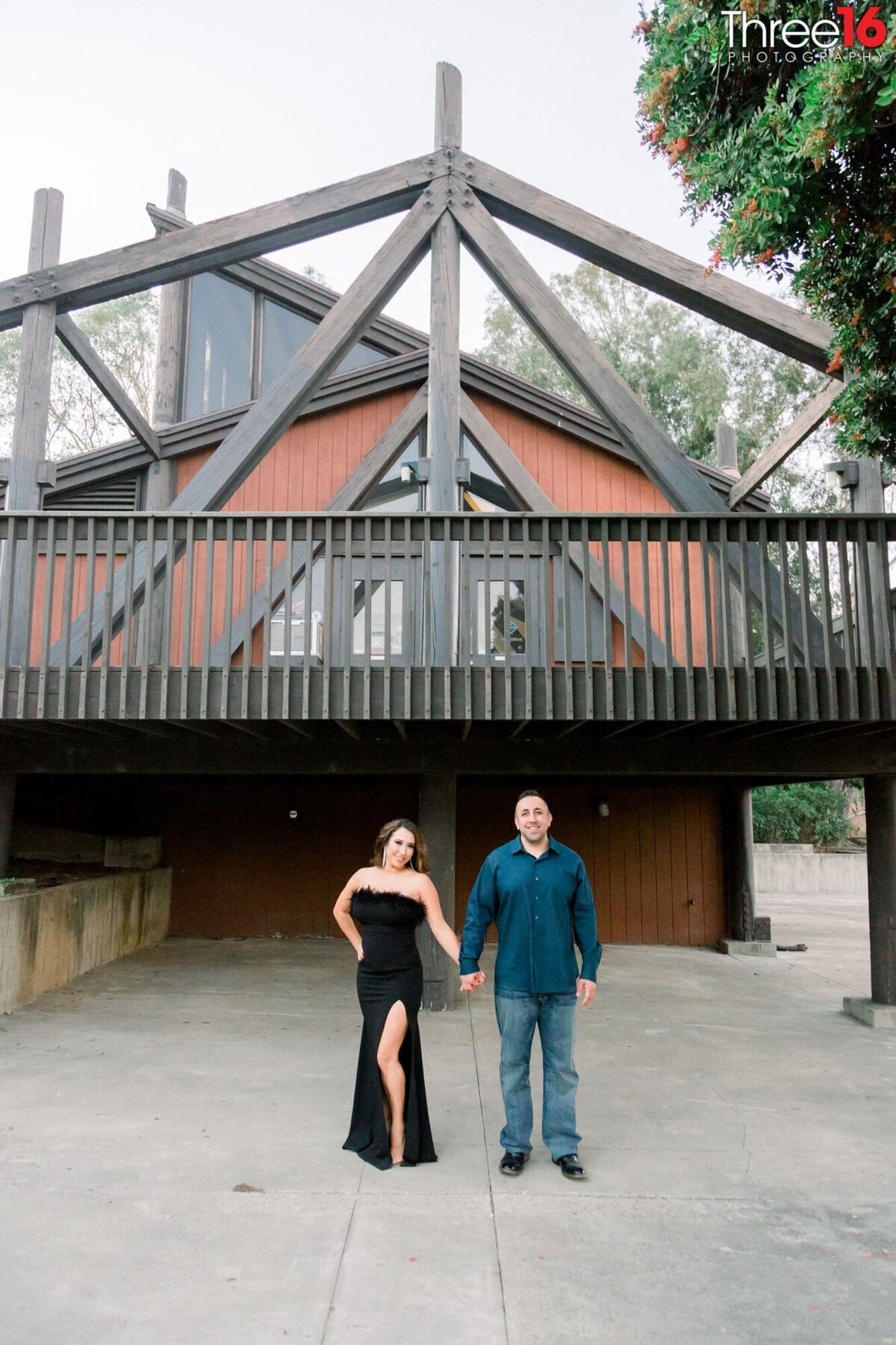 Engaged couple hold hands in front of building during photo session at Laguna Niguel Regional Park