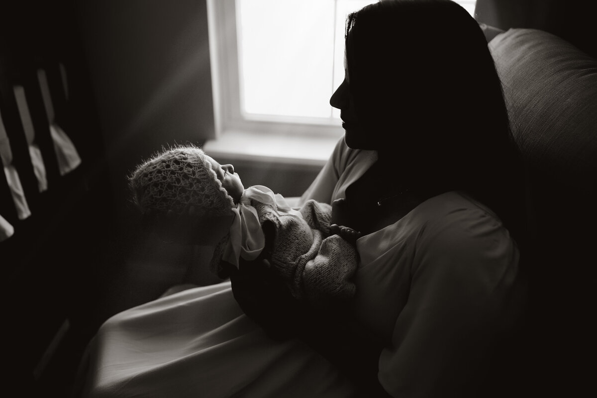 incredible dark and moody black and white portrait of a mother in a rocking chair holding her newborn daughter white she sleeps
