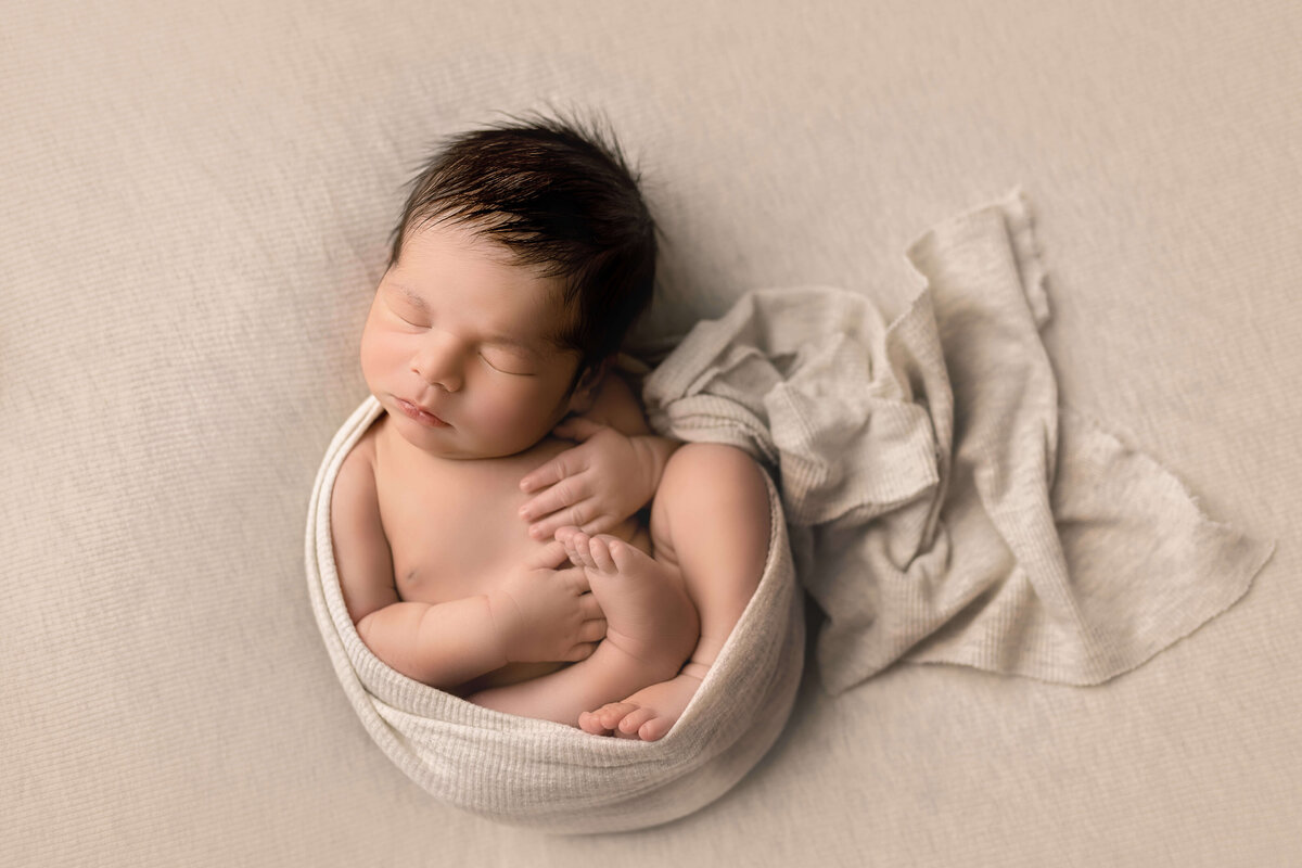 Newborn boy wrapped in ivory swaddle