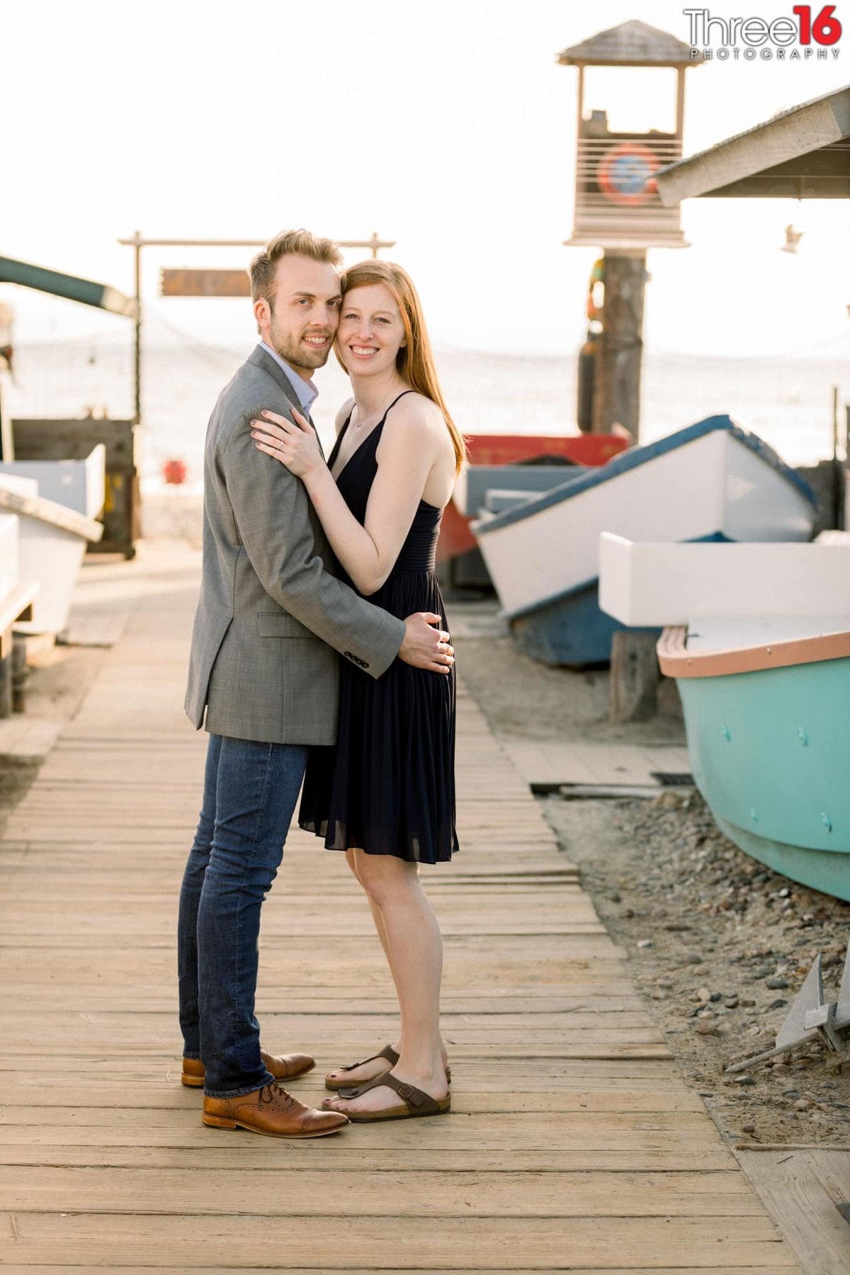 Engaged couple cuddle up as they pose for photos on a small dock in Newport Beach