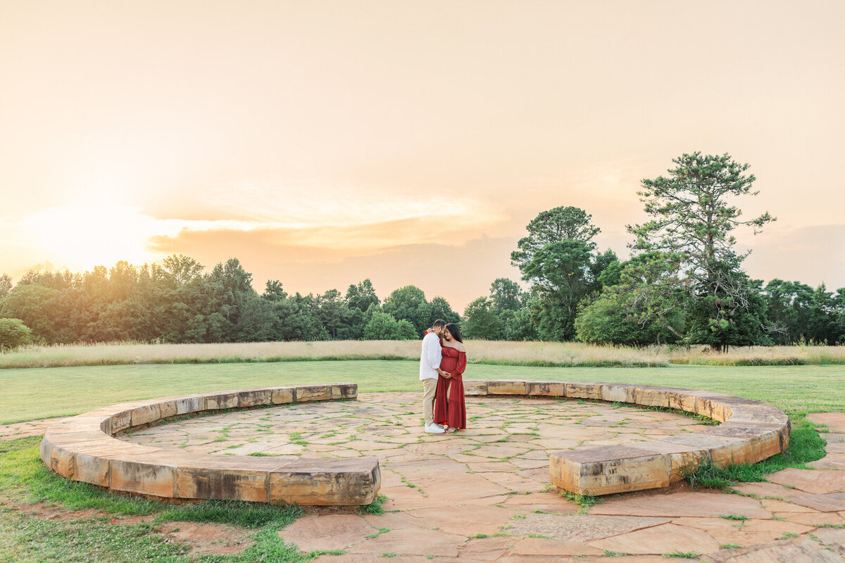 Pregnant mama and dad embrace in field at sunset