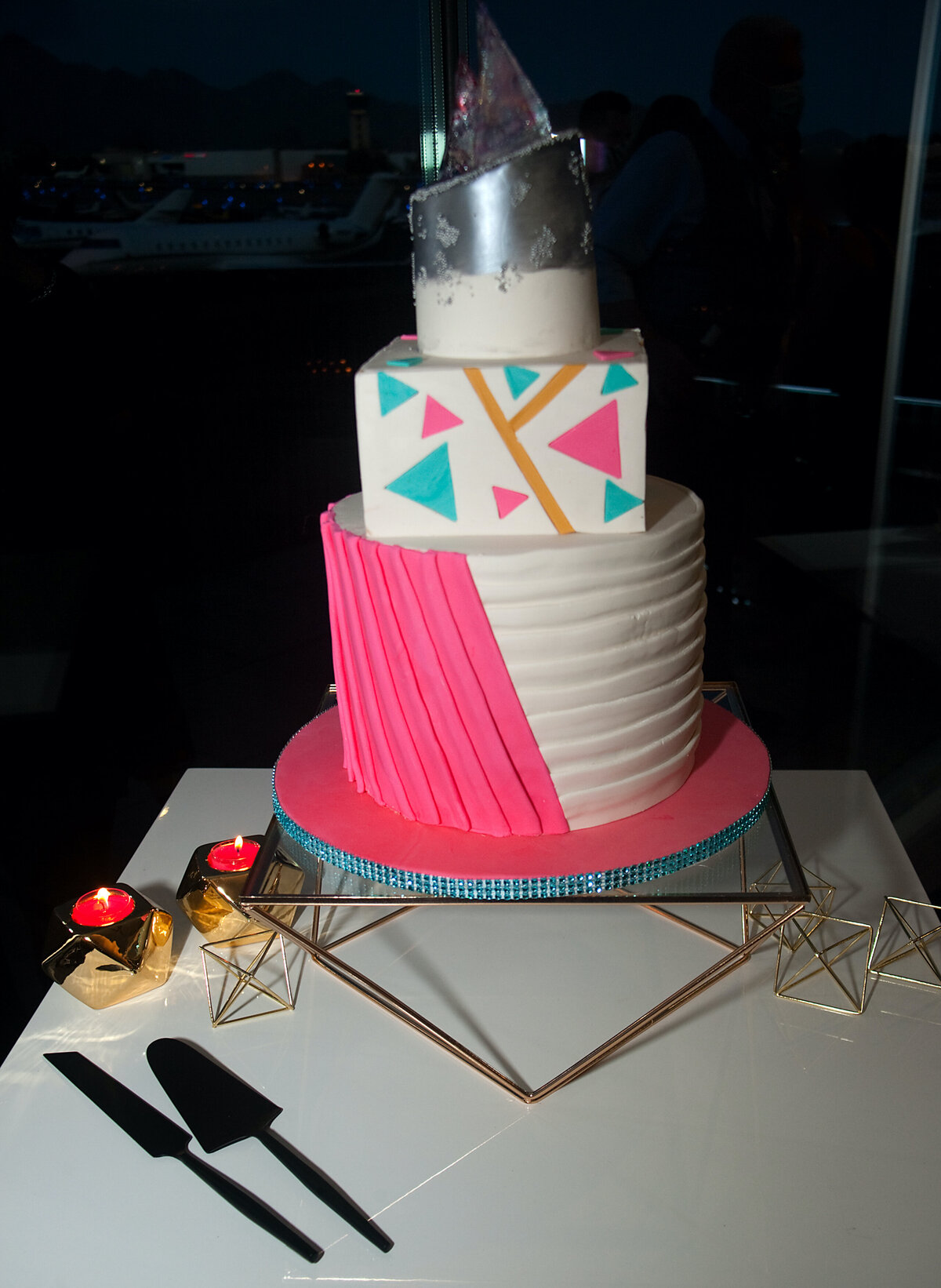 Geometric 3 tier wedding cake - tall round bottom tier with hot pink and white pleats; square middle tier with teal , gold, pink triangle accents; white and silver top tier carved at an angle and embellished with poured sugar triangle accents.