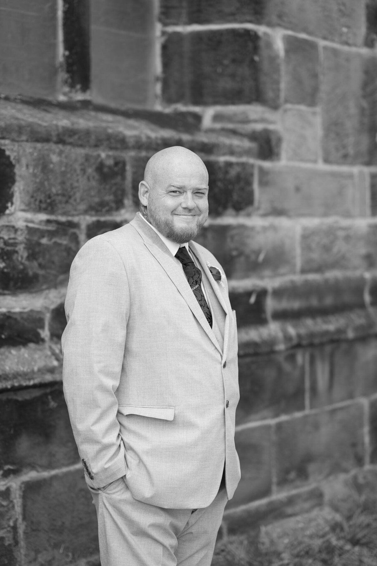 Groom smiling in wedding suit against church stone wall – Cheshire wedding portrait.