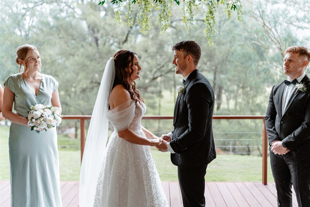 A radiant bride, clutching a bouquet of ivory roses, exchanges heartfelt vows with her groom under a cascading arch of fragrant blooms.