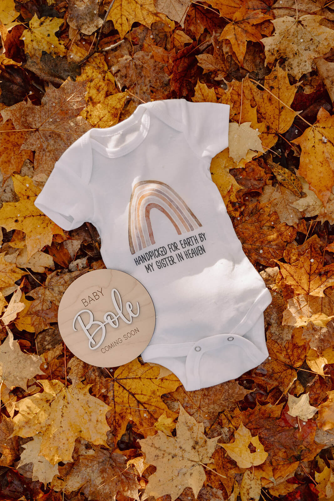 Baby onesie and annoucement card laying in leaves
