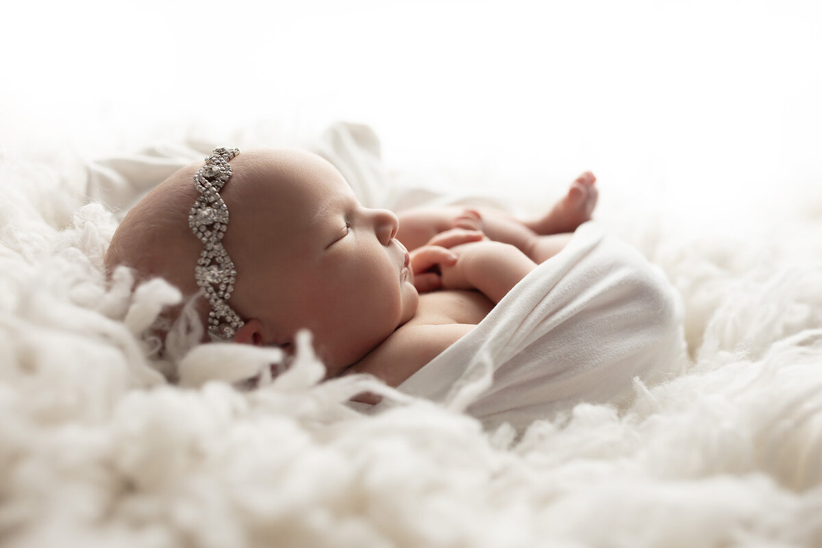 Close-up side profile of a sleeping baby girl wearing a rhinestone headband, beautifully photographed by a luxury newborn photography studio.