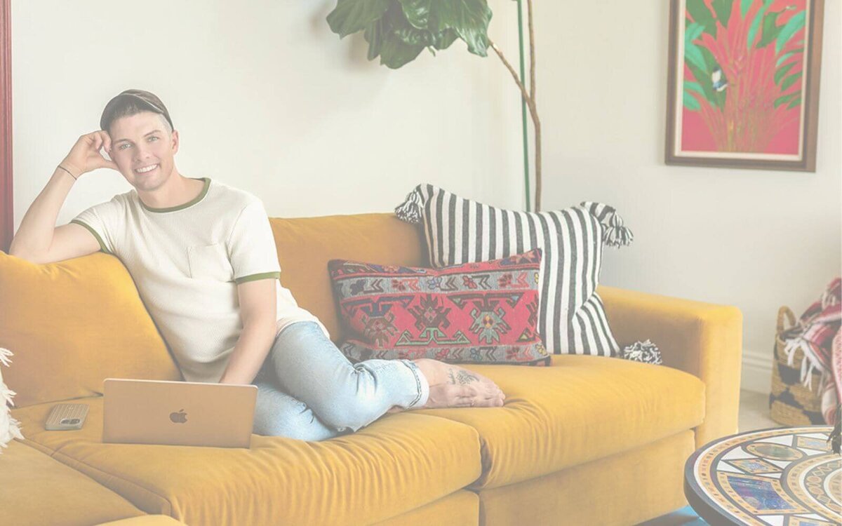 Madison Wetter, Cave Creek real estate agent, sitting on mustard yellow sofa with laptop, smiling in a modern desert-inspired living room