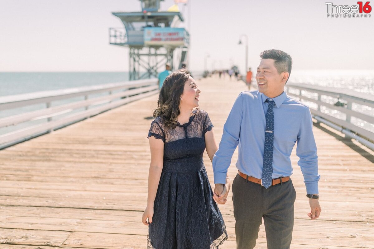 Engaged couple share a laugh while walking on the San Clemente Pier