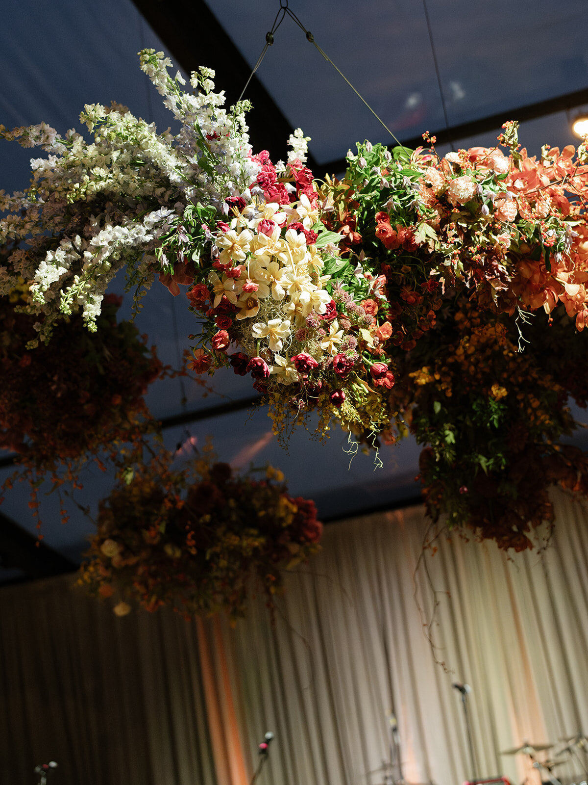 Interacting and sculptural floral clouds hang over the dance floor and bars of this fall wedding reception in Tennessee. Clear top tent build out for fall wedding reception in Tennessee hills.  Product clustered floral clouds in a tasteful fall color palette of copper, ruby, gold, burgundy, rust, and lavender. Orchids, bittersweet berries, butterfly ranunculus, and tulips are highlighted. Unique floral design with flower forward large scale installations. Design by Rosemary & Finch Floral Design in Nashville, TN.