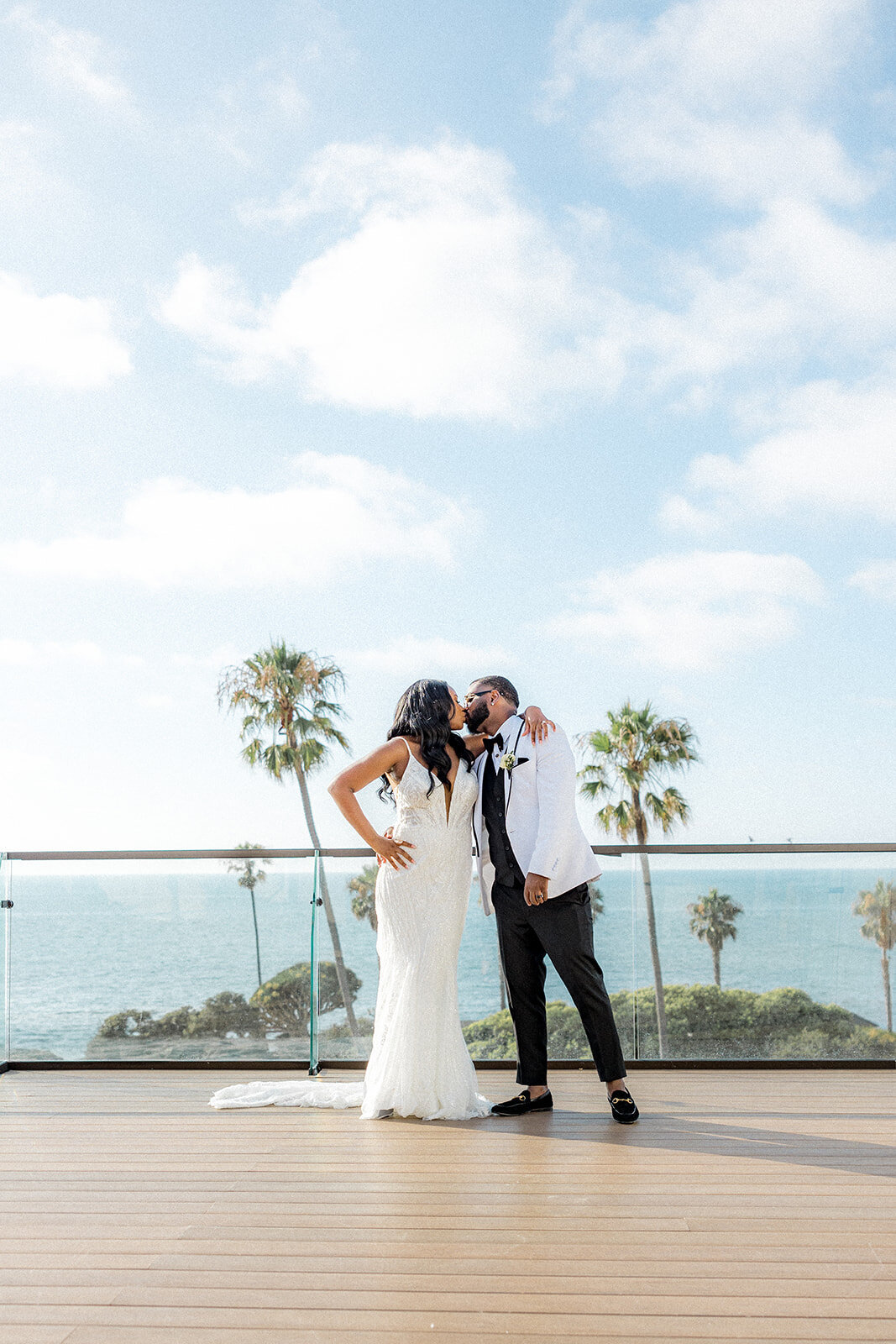 Bride and groom kissing with palm trees and ocean in back in San Diego