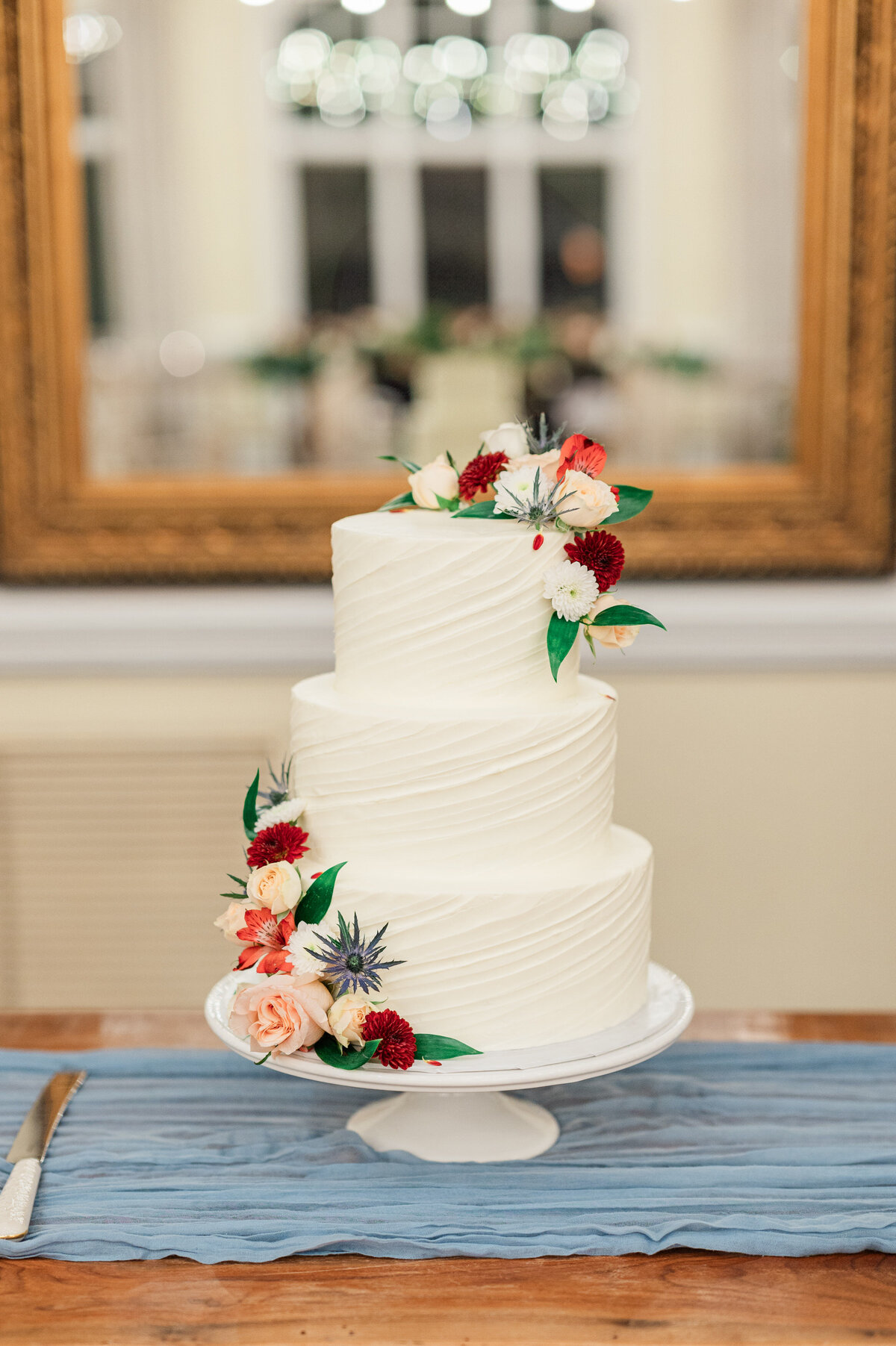 A simple three tiered white wedding cake with flowers around it