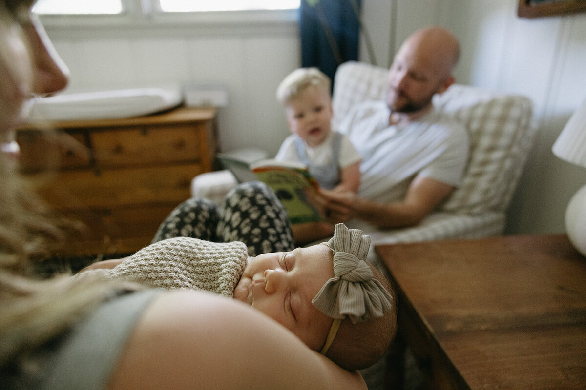 Newborn baby photographed while her mother holds her and her father and brother look on.  