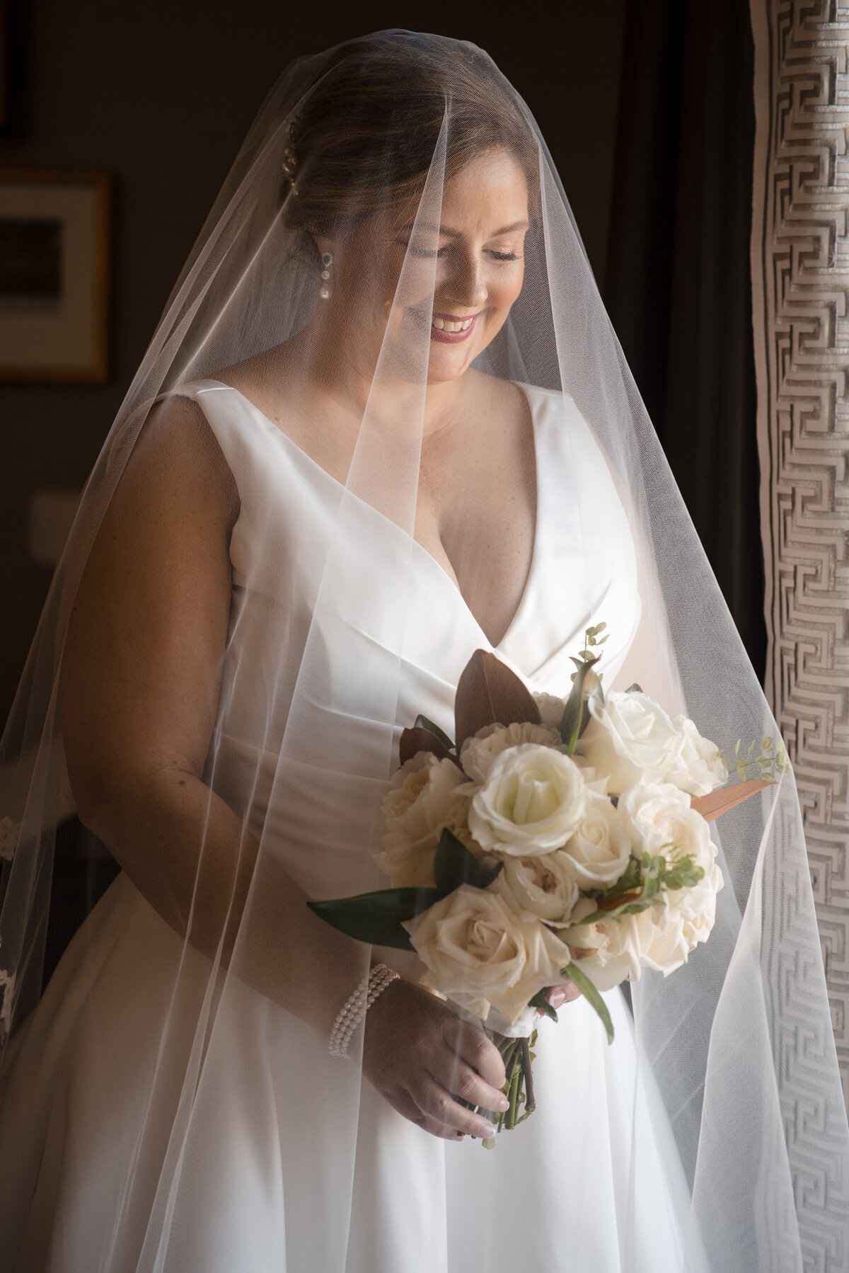 Bridal portrait where the bride has her veil over her face and she's looking down smiling at her flowers at the Ballantyne by Charlotte wedding photographer DeLong Photography