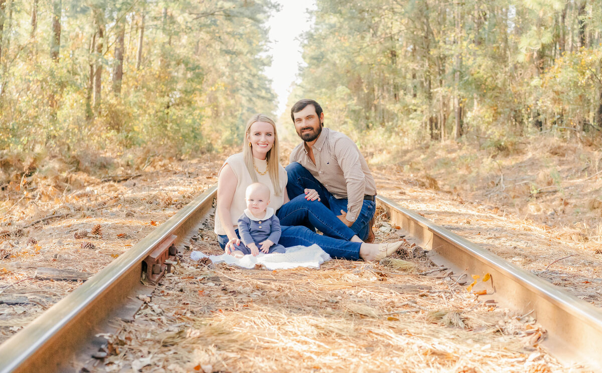 mom, dad, and baby sitting on blanket on ground in tall trees on family property