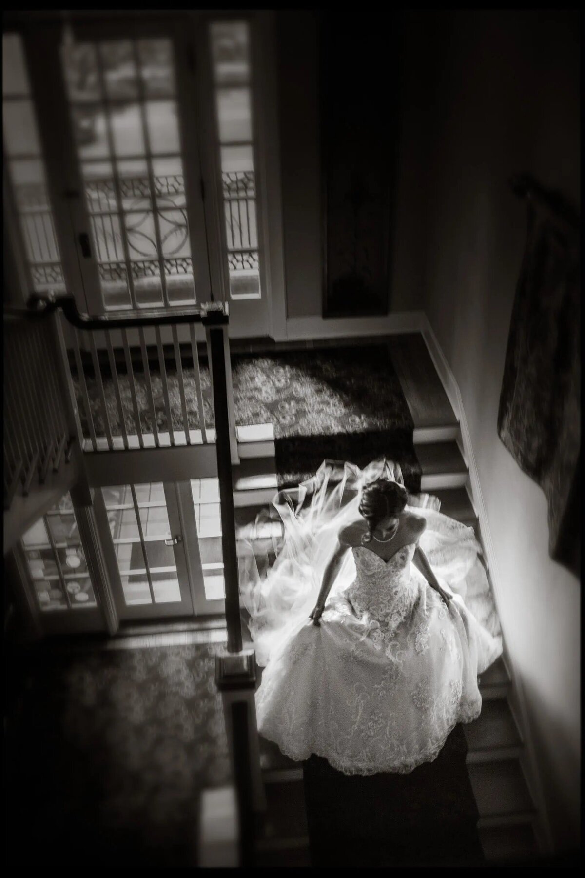 Bride elegantly descending a staircase, her gown and veil cascading behind her in a black and white photo