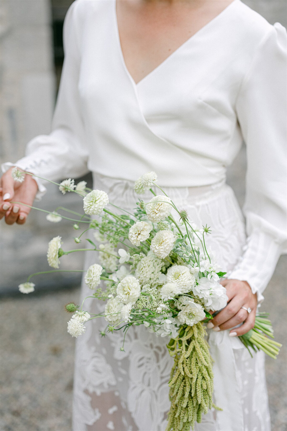 A bride grips a modern bouquet of white flowers and lush greenery at a Montreal wedding.