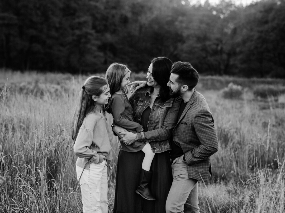 mom dad and two daughters posing in field for family photos