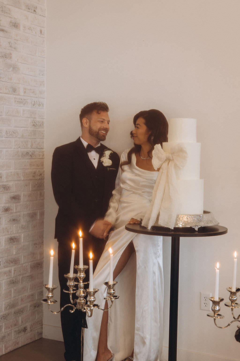 A newlywed couple holding hands and standing next to their cake.