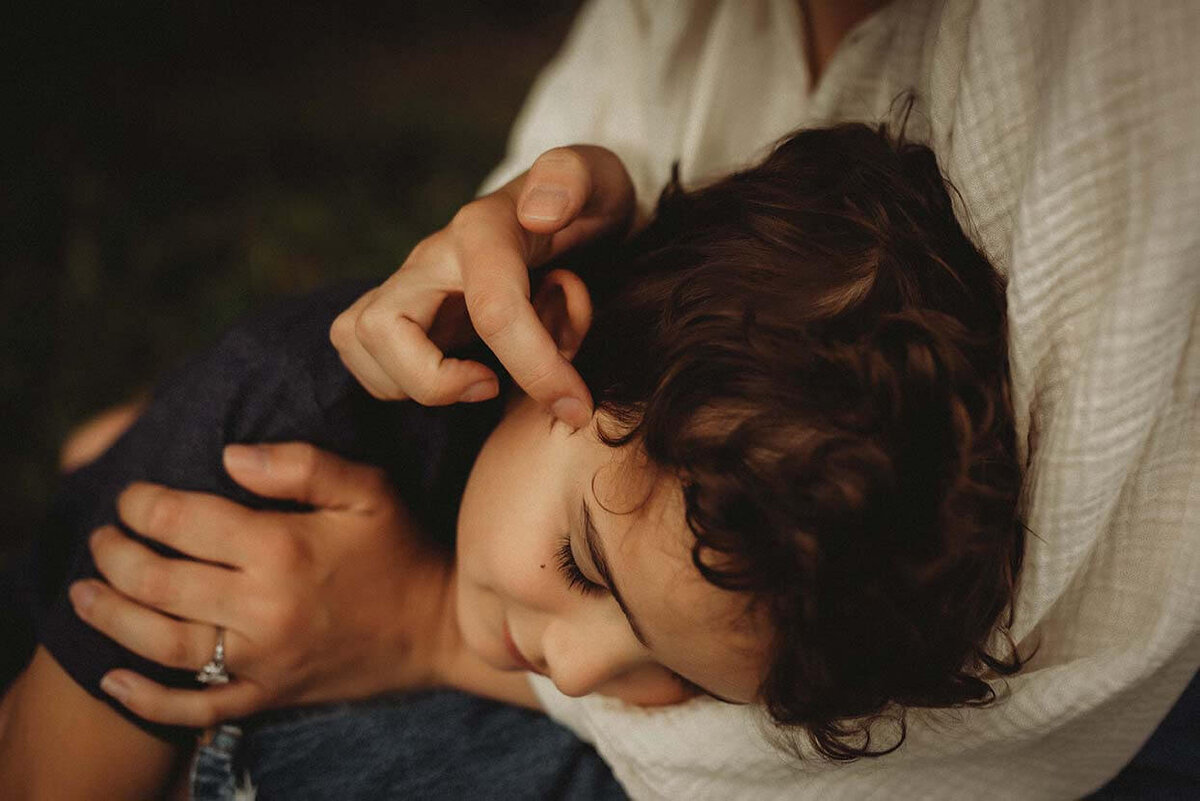 A mother cradles her sons head in her lap while gently playing with his curly hair