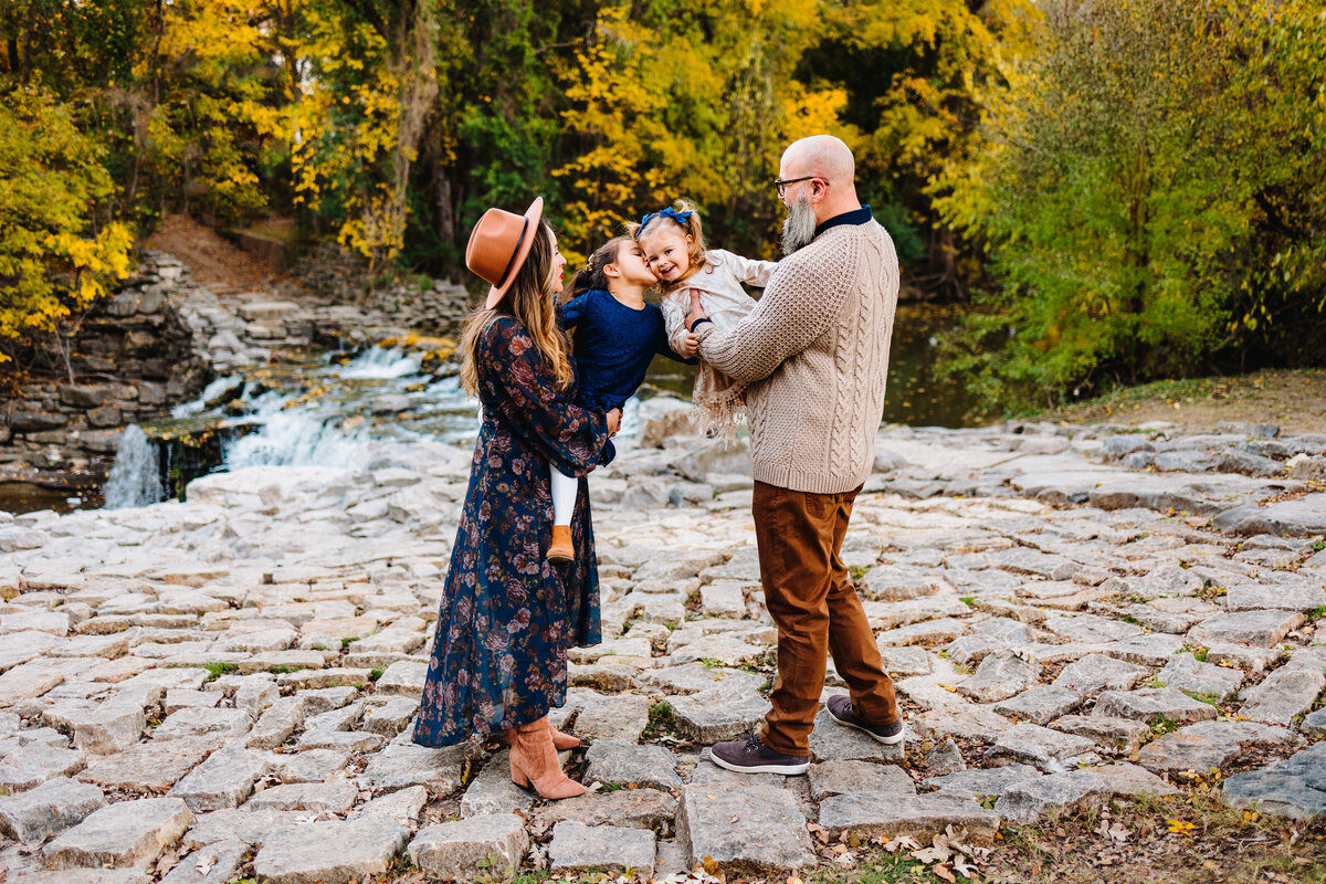 Best family photography services in Albuquerque capture a heartwarming moment with parents lovingly carrying their daughters. The family is dressed in vintage outfits, including long dresses, orange pants, and sweaters.