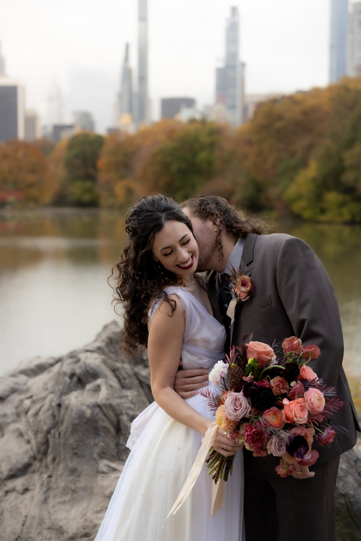 The couple holding hands and smiling as they walk through a peaceful Central Park path.
