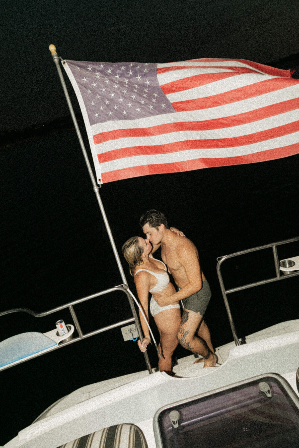 A engagement couple kissing on a boat with the American flag in the background. 