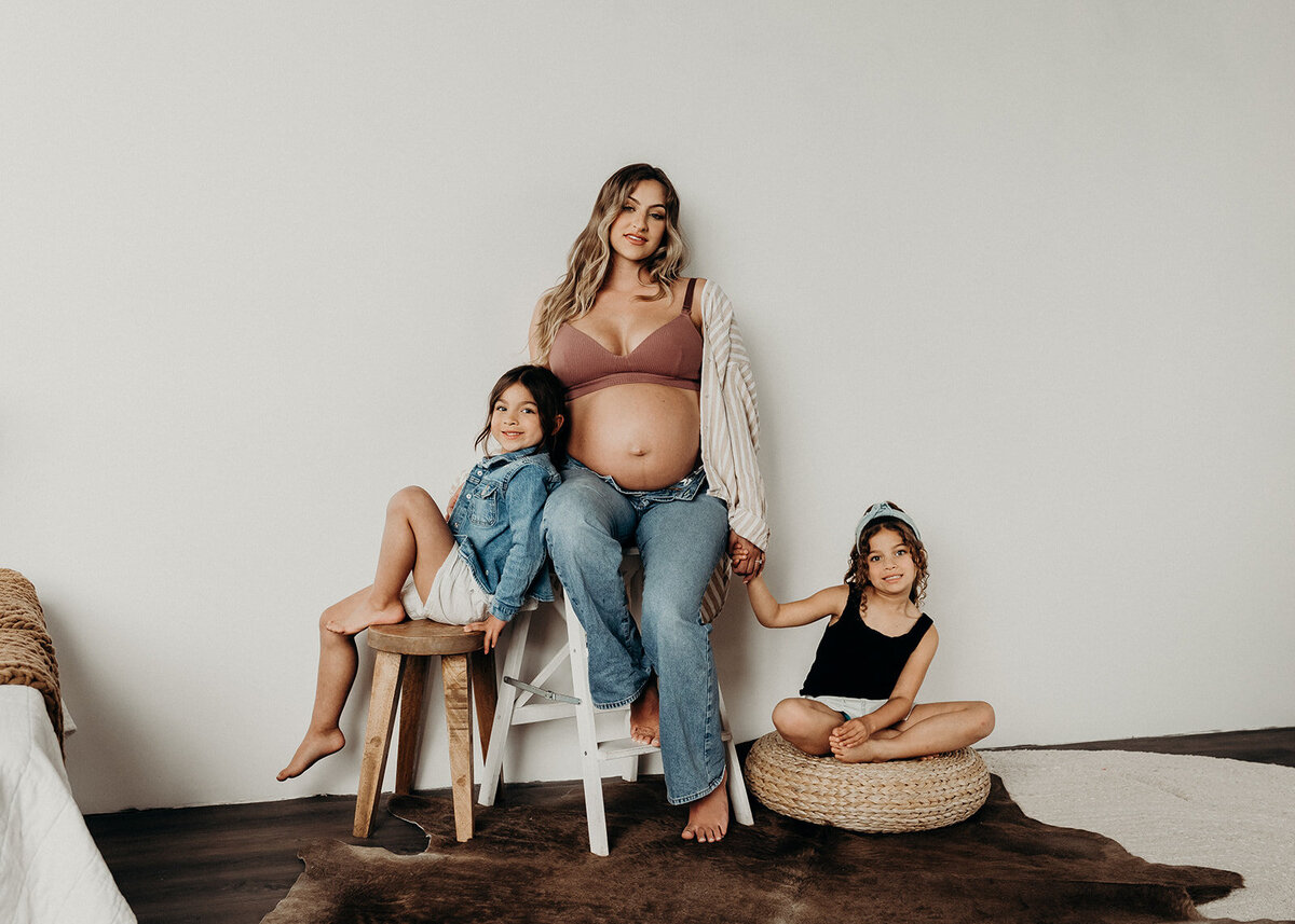 maternity photo of Denver mom holding her 2 daughters hands