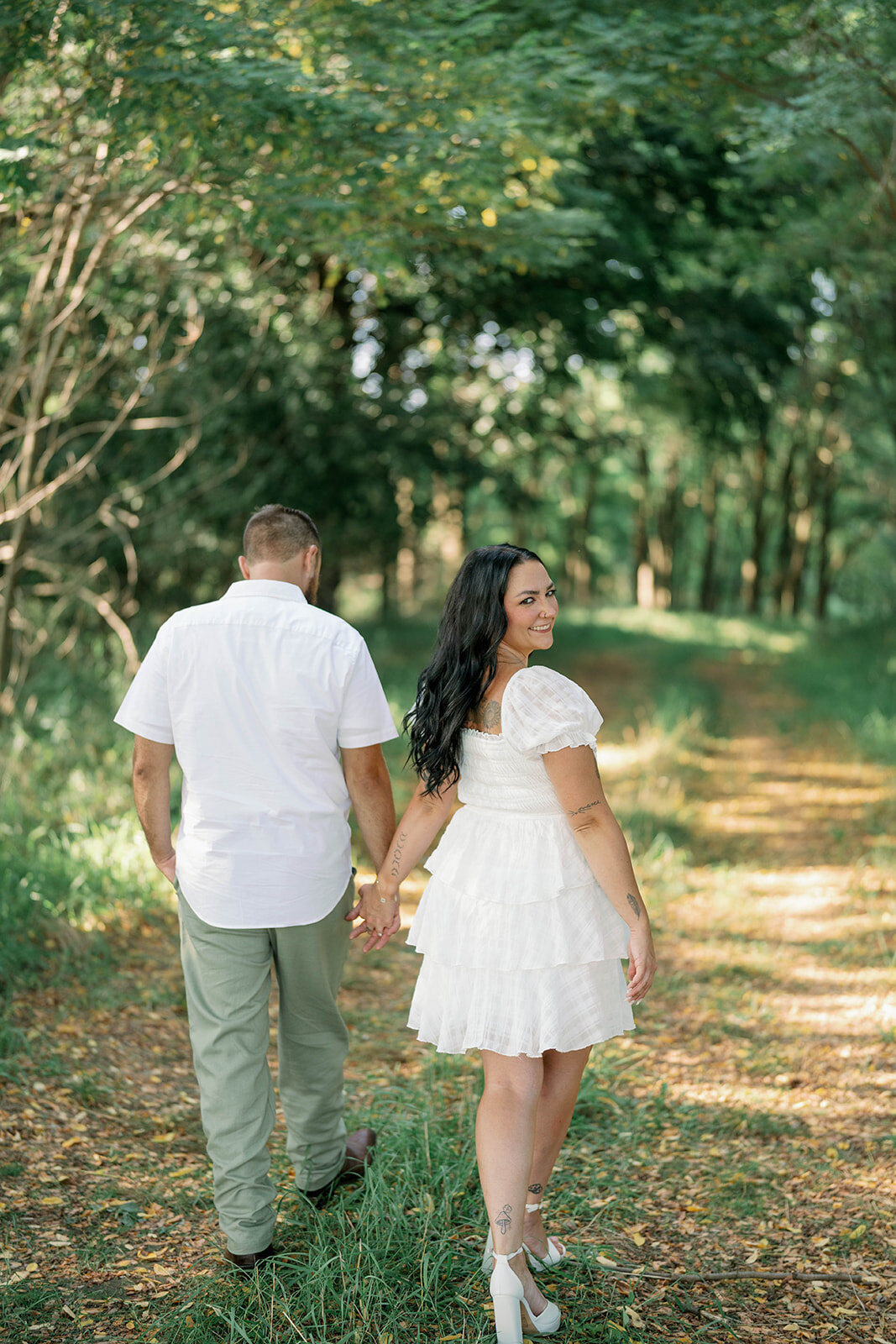 Kali and Joe walking hand in hand down a shaded wooded trail on private property during their Detroit engagement session.